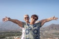 Happy couple of women standing on hill with mountain and city on background looking at camera with arms raised - active seniors Royalty Free Stock Photo