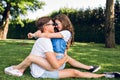 Happy couple of young people on grass in summer park. Pretty girl with long curly hair in jeans clothes is sitting on Royalty Free Stock Photo