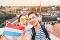 Happy couple of young people hug and take selfies with the flag of Luxembourg while sightseeing in old town. Tourism,