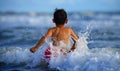 Happy and crazy excited child running free towards sea horizon having fun on the beach playing splashing on water enjoying