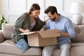 Happy curious couple unpacking parcel at home, sitting on couch