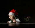 Happy curious infant boy toddler in red Santa hat and white - green clothes is lying on floor looking at copy space Royalty Free Stock Photo