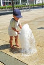 Happy curious toddler boy playing with bucket in water of fountain