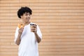 Happy curly-haired afro guy holding an orange donut and a cup of coffee, looking at copy space Royalty Free Stock Photo