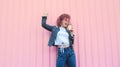 Happy curly haired woman in denim clothes with pink hair  drinking coffee on pink background. Royalty Free Stock Photo