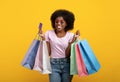 Happy customer. Joyful black lady with shopping bags and unlimited credit card smiling over yellow background Royalty Free Stock Photo