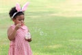 Happy cute African girl with black curly hair wearing bunny ears blowing soap bubbles in green nature garden. Kid spending time Royalty Free Stock Photo