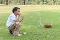 Happy cute Asian boy blowing soap bubbles while sitting on green grass in nature garden park. Kid spending time outdoors in meadow Royalty Free Stock Photo