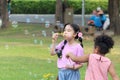 Happy cute Asian girl with curly hair African friend blowing soap bubbles in green nature garden. Kids spending time outdoor Royalty Free Stock Photo