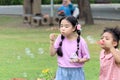 Happy cute Asian girl with curly hair African friend blowing soap bubbles in green nature garden. Kids spending time outdoor Royalty Free Stock Photo