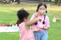 Happy cute Asian girl with curly hair African friend blowing soap bubbles in green nature garden. Kids spending time outdoor Royalty Free Stock Photo