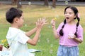 Happy cute Asian girl with friend blowing bubbles in green nature garden. Kids spending time outdoor together in meadow. Cute Royalty Free Stock Photo