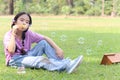 Happy cute Asian girl with pigtails blowing soap bubbles while sitting on green grass in nature garden park. Kid spending time Royalty Free Stock Photo
