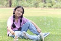 Happy cute Asian girl with pigtails blowing soap bubbles while sitting on green grass in nature garden park. Kid spending time Royalty Free Stock Photo