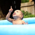 Happy cute baby boy in blue inflating pool pointing up Royalty Free Stock Photo