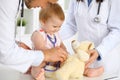 Happy cute baby at health exam at doctor`s office. Toddler girl is sitting and keeping stethoscope and teddy bear