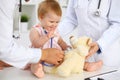 Happy cute baby at health exam at doctor`s office. Toddler girl is sitting and keeping stethoscope and teddy bear