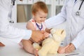 Happy cute baby at health exam at doctor`s office. Toddler girl is sitting and keeping stethoscope and teddy bear