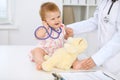 Happy cute baby at health exam at doctor`s office. Toddler girl is sitting and keeping stethoscope and teddy bear Royalty Free Stock Photo