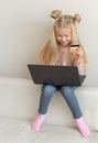 Happy cute caucasian little girl holding credit card buying online sitting on the couch Royalty Free Stock Photo