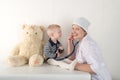 Happy cute boys playing with stethoscope in doctors office, hugging plush toy bear and smiling at camera. Female pediatrics. Copy Royalty Free Stock Photo
