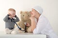 Happy cute boys playing with stethoscope in doctors office, hugging plush toy bear and smiling at camera. Female pediatrics. Copy