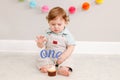 Happy cute Caucasian baby boy celebrating first birthday at home. Child kid toddler sitting on floor in room. Tasty cupcake Royalty Free Stock Photo