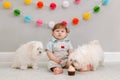 Happy cute Caucasian baby boy celebrating first birthday at home. Child kid toddler sitting on a floor with two white pet dogs Royalty Free Stock Photo