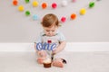 Happy cute Caucasian baby boy celebrating his first birthday at home. Child kid toddler sitting on floor in room. Tasty cupcake Royalty Free Stock Photo