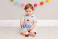 Happy cute Caucasian baby boy celebrating his first birthday at home. Child kid toddler sitting on floor in room. Tasty cupcake Royalty Free Stock Photo