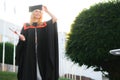 Happy cute caucasian grad girl is smiling. She is in a black mortar board, with red tassel, in gown, with nice brown Royalty Free Stock Photo