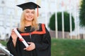 Happy cute caucasian grad girl is smiling. She is in a black mortar board, with red tassel, in gown, with nice brown Royalty Free Stock Photo