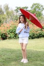 Happy and cute child girl holding red umbrella in park with green trees and flowers Royalty Free Stock Photo