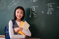 Happy cute child girl student carrying a backpack and holding books with looking at camera in the classroom at school Royalty Free Stock Photo