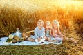 Happy cute children are having a picnic in a summer wheat field with a white pigeon. Beautiful two girls and a boy eat bread and Royalty Free Stock Photo