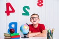 Happy cute clever boy is sitting at a desk in a glasses with rai Royalty Free Stock Photo