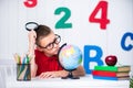 Happy cute clever boy is sitting at a desk in a glasses with raising hand. Child is ready to answer with a blackboard on Royalty Free Stock Photo