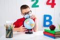 Happy cute clever boy is sitting at a desk in a glasses with raising hand. Child is ready to answer with a blackboard on Royalty Free Stock Photo