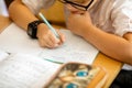 Happy cute clever boy is sitting at a desk in a glasses with raising hand. Child is ready to answer with a blackboard on a Royalty Free Stock Photo