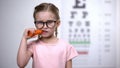 Happy cute girl in eyeglasses eating carrot, vitamin A for good vision, health Royalty Free Stock Photo