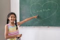 Happy cute girl using chalk drawing heart and write love mom on chalkboard wall in classroom at elementary school Royalty Free Stock Photo