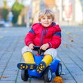 Happy cute kid boy in colorful fashion clothes driving toy car. child having fun, outdoors. Active children leisure in Royalty Free Stock Photo