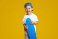 Happy cute kid wearing white t-shirt and blue cap while holding longboard and smiling Royalty Free Stock Photo