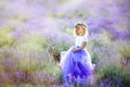 Happy cute little blonde curly girl wearing lavender dress and wreath in lavender field holding her skirt with violet flowers Royalty Free Stock Photo