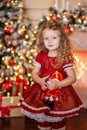 Happy cute little blonde girl with long hair in a red dress, waiting for Christmas and New year opens a gift on the Royalty Free Stock Photo