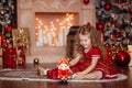 Happy cute little blonde girl with long hair in a red dress, waiting for Christmas and New year opens a gift on the Royalty Free Stock Photo