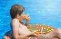 Happy cute little boy teenager lying on inflatable donut ring with orange in swimming pool. Active games on water, vacation Royalty Free Stock Photo