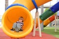 Happy cute little child boy having fun on a yellow slide outdoor in the park, sunny summer day in children playground. Royalty Free Stock Photo