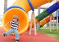 Happy cute little child boy having fun on a yellow slide outdoor in the park, sunny summer day in children playground. Royalty Free Stock Photo