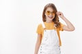 Happy cute little fashionable girl, daughter wearing yellow round sunglasses, t-shirt and dungarees, put on glasses and